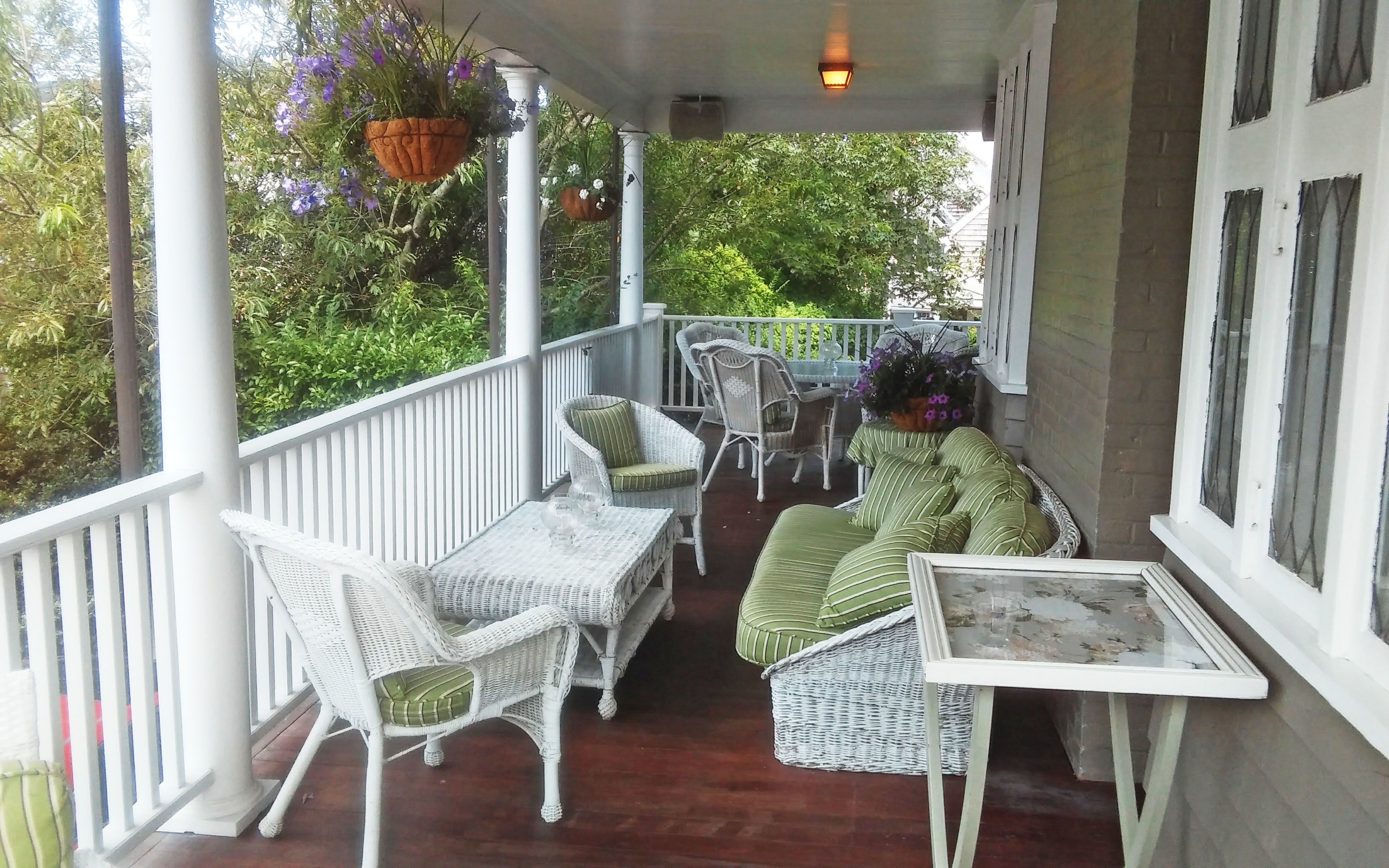 A covered porch with wicker furniture, a table, and hanging flower baskets.