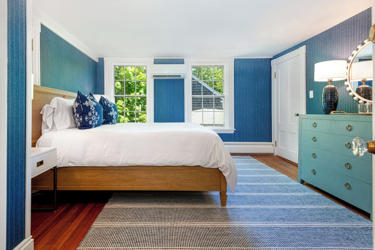 A bedroom with a bed, dresser, and a window with a view of trees.