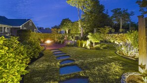 A well-lit garden pathway with stepping stones, surrounded by lush greenery and a stone wall. - Martin House Inn (Nantucket)