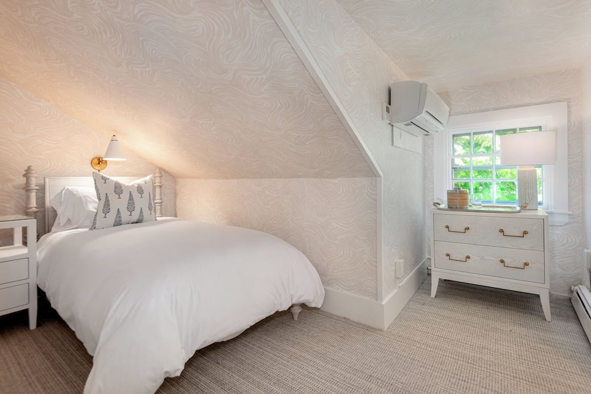 A bedroom with a bed, nightstand, dresser, and a window with a view of greenery.