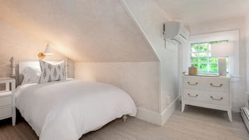 A bedroom with a bed, nightstand, dresser, and a window with a view of greenery.