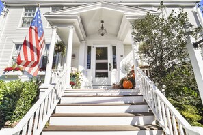 A white house with a front porch, a flag, and a number '61' on the door.