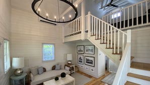 A spacious living room with a high ceiling, a staircase, and a large chandelier. - Martin House Inn (Nantucket)