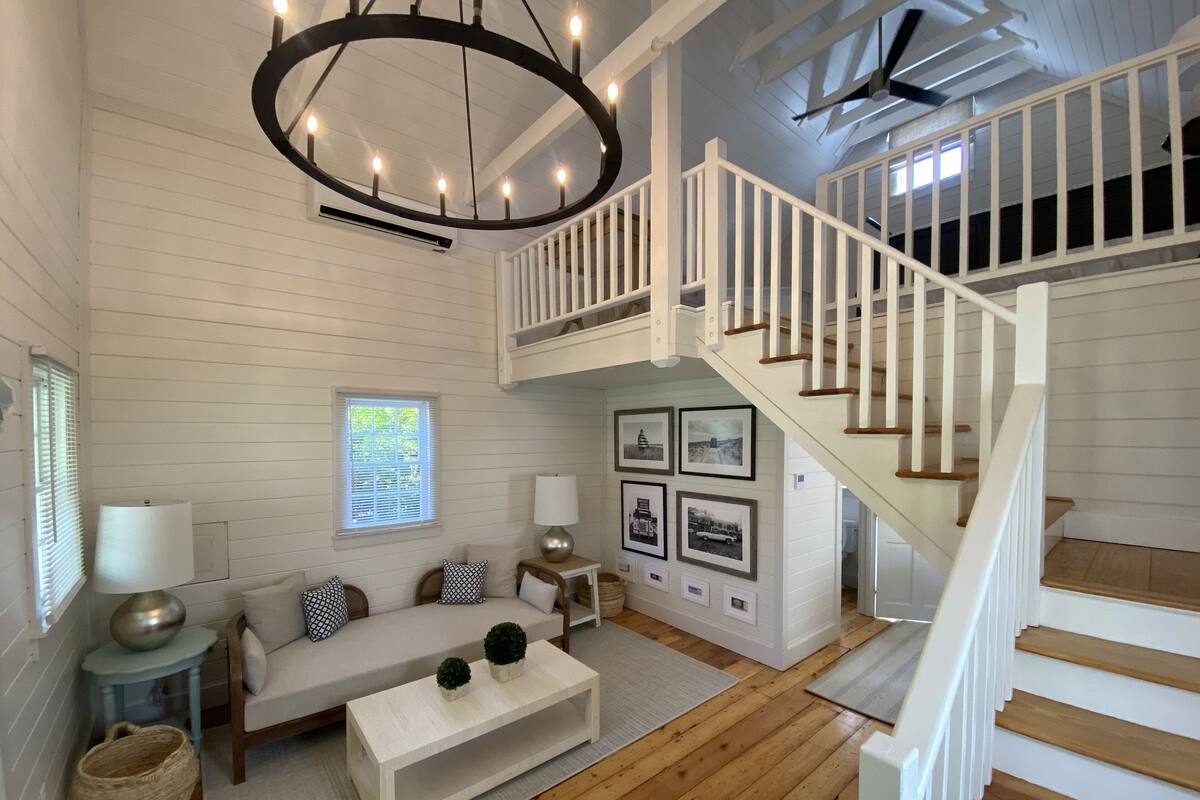 A spacious living room with a high ceiling, a staircase, and a large chandelier.