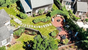 An aerial view of a residential area with a house featuring a stone facade, a circular patio with seating, and a small garden area. - Martin House Inn (Nantucket)