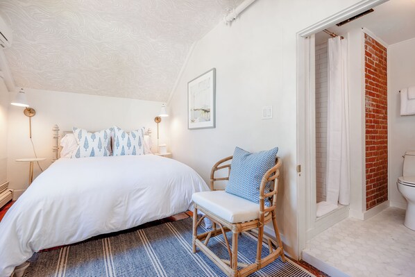 A bedroom with a bed, a chair, a wall-mounted picture, and a door leading to a bathroom. - Martin House Inn (Nantucket)