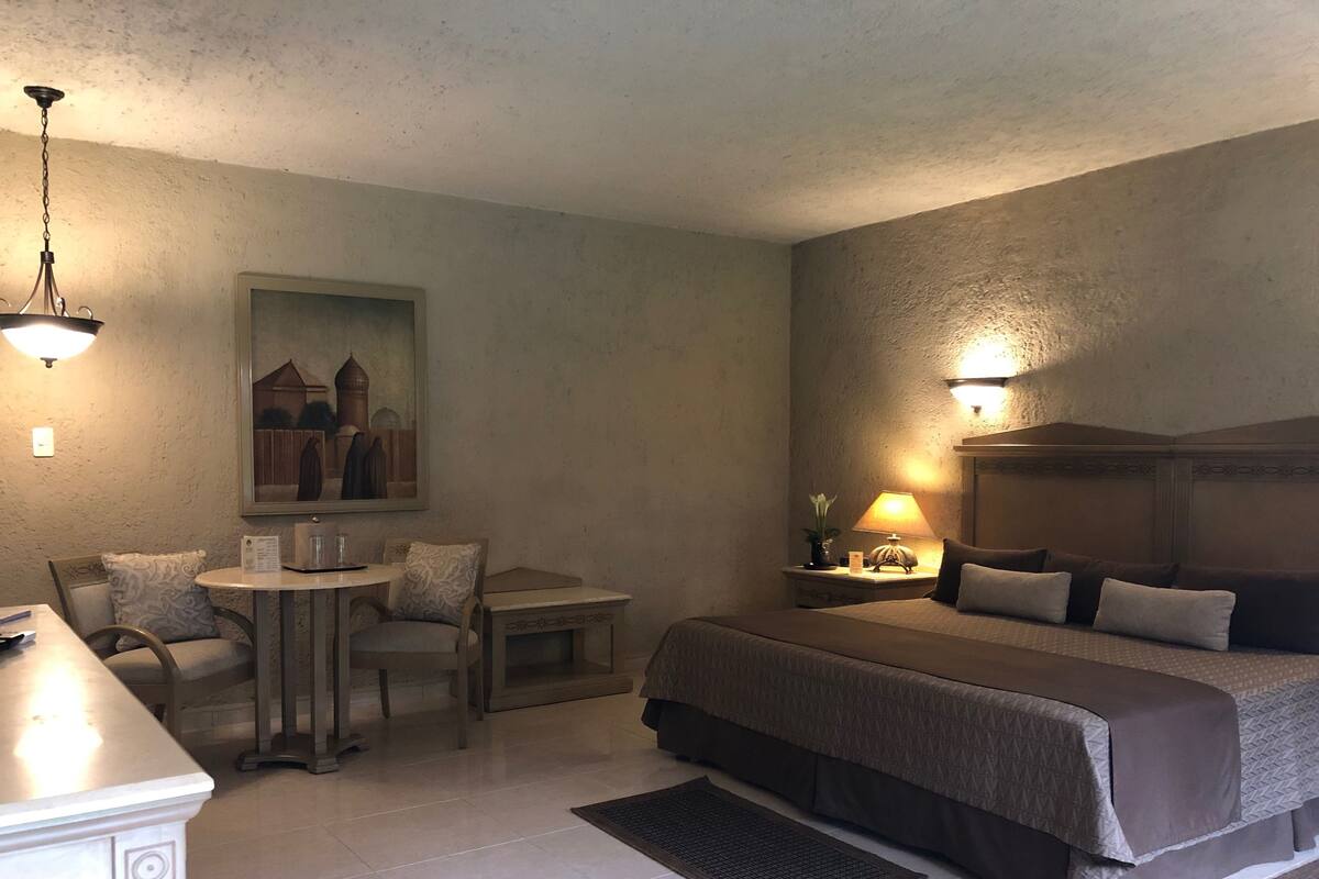 Une chambre d’hôtel avec un lit, un bureau, une chaise, une lampe et un tableau au mur.