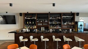 Een bar met meerdere flessen en glazen op planken, barstoelen en een flatscreen aan de muur.