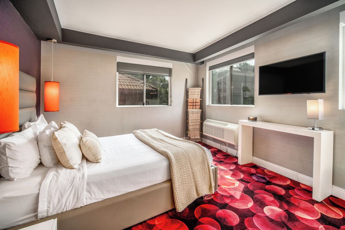 Een moderne hotelkamer met een groot bed, een flatscreen televisie aan de muur en een levendig rood tapijt met een patroon.