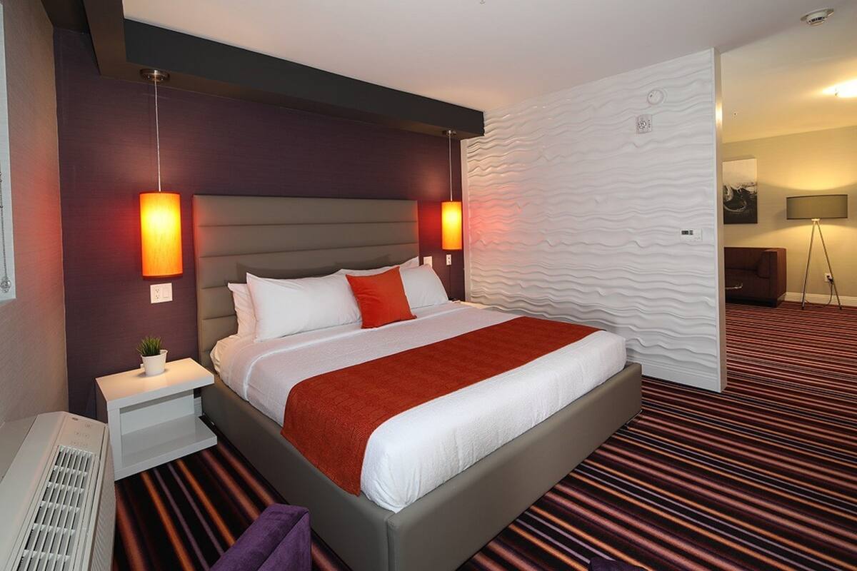 Une chambre d’hôtel moderne avec un grand lit, une table de chevet, un radiateur et une lampe fixée au mur.