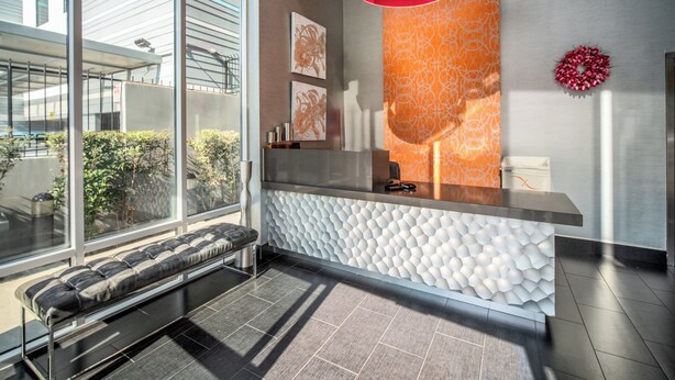 A modern reception area with a bench, a reception desk, and a patterned wall. - Lexen Hotel- Hollywood Walk of Fame/Universal Studios (Los Angeles)