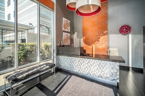 Een moderne receptiezone met een bank, een receptiebalie en een behang met patroon.