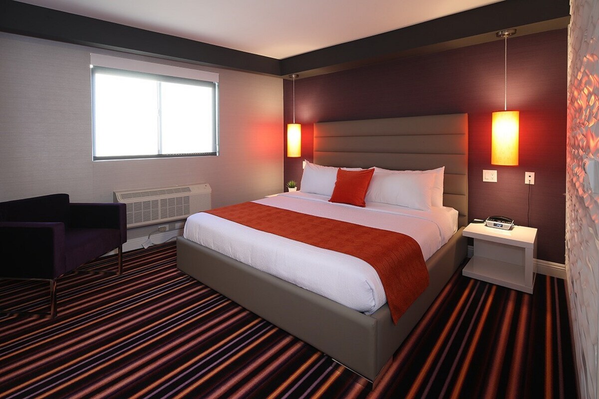 Une chambre d’hôtel avec un grand lit, deux tables de chevet, une chaise, un radiateur et une fenêtre.