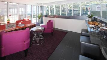 Un hall d’hôtel moderne, doté d’espaces aménagés avec des sièges, d’un bar et de grandes fenêtres offrant une vue sur la ville.