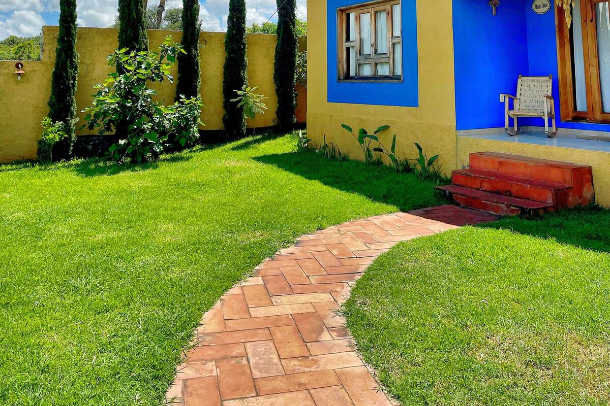 Un edificio amarillo con detalles azules, un camino de ladrillo y altos cipreses.