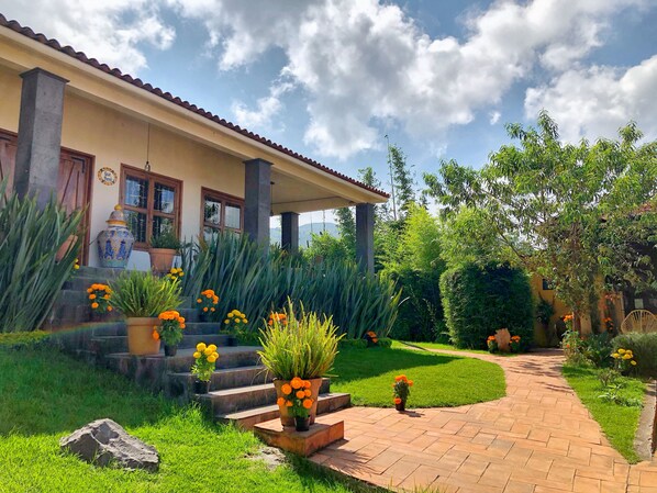 Una casa con techo de tejas, un porche con escalones y un jardín con macetas y flores.