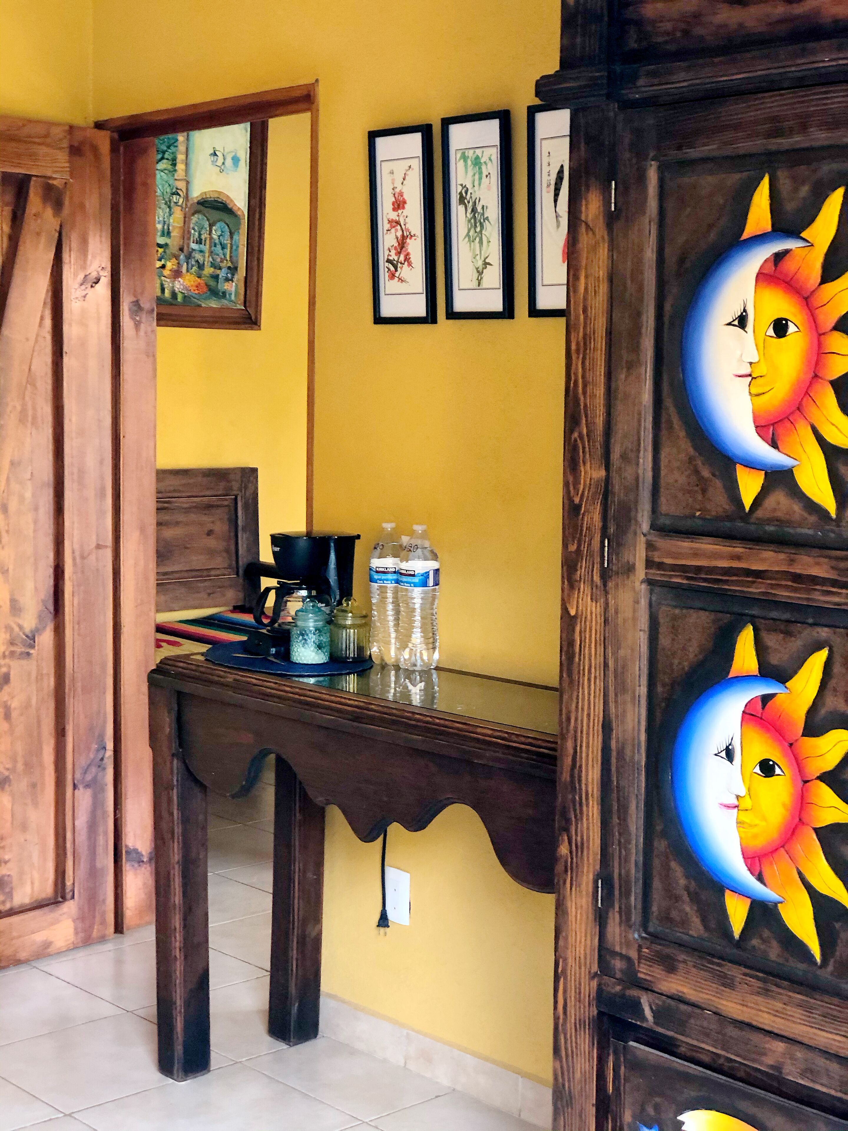A room with a wooden table, a yellow wall, and framed artwork.