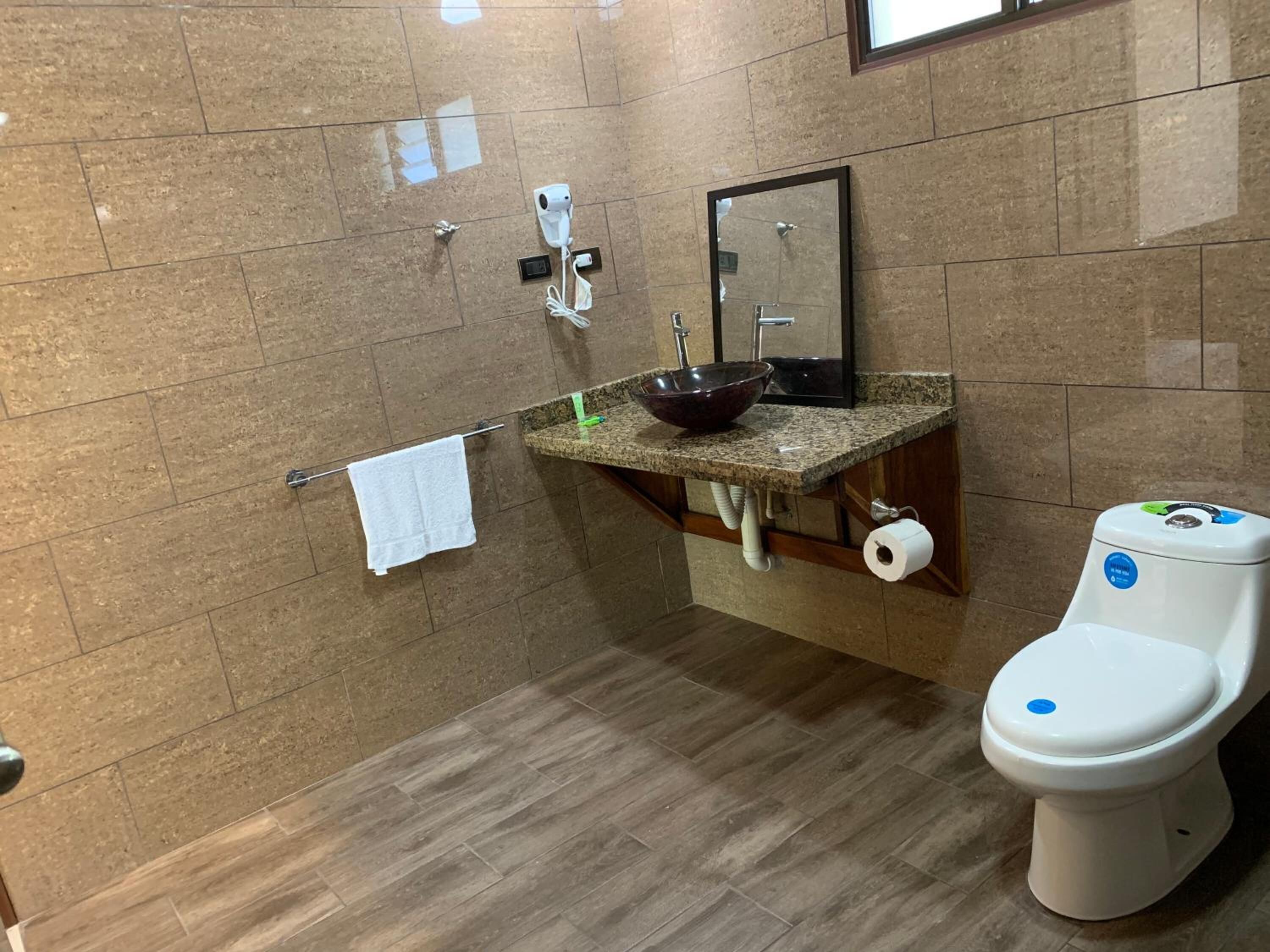 A bathroom with a marble-tiled wall, a sink with a bowl, a mirror, a towel rack, and a toilet.