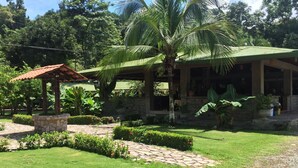 A well-maintained garden with a stone gazebo, palm trees, and a covered structure with a stone facade. - Hotel Manuel Antonio Park (Quepos)