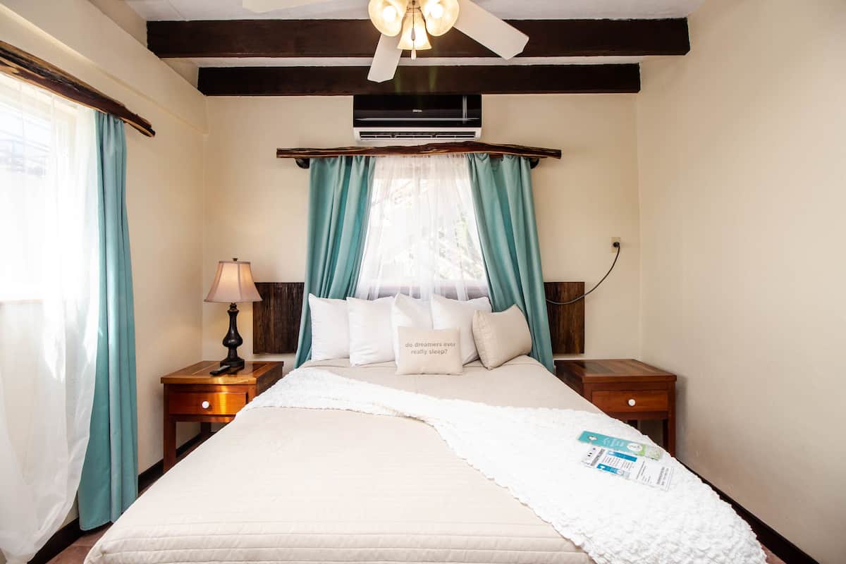 A neatly made bed with a white comforter, a bedside lamp, and a bedside table with a book.