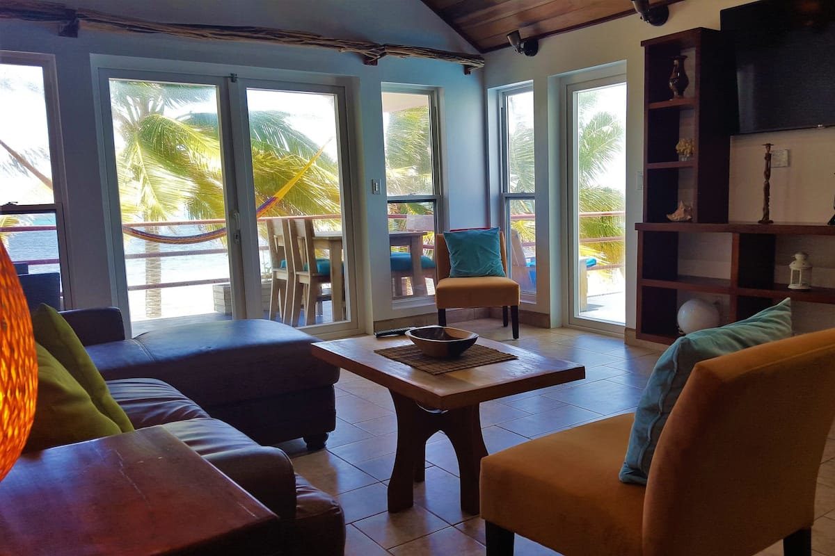 A room with a wooden table, two sofas, a chair, a TV, and a bookshelf.