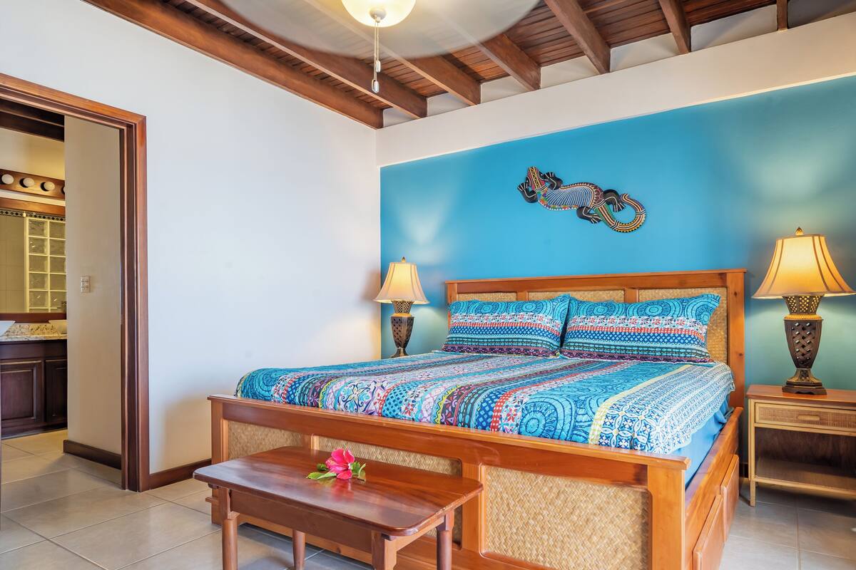 A bedroom with a wooden bed, two bedside lamps, a decorative wall piece, and a small table with a flower.