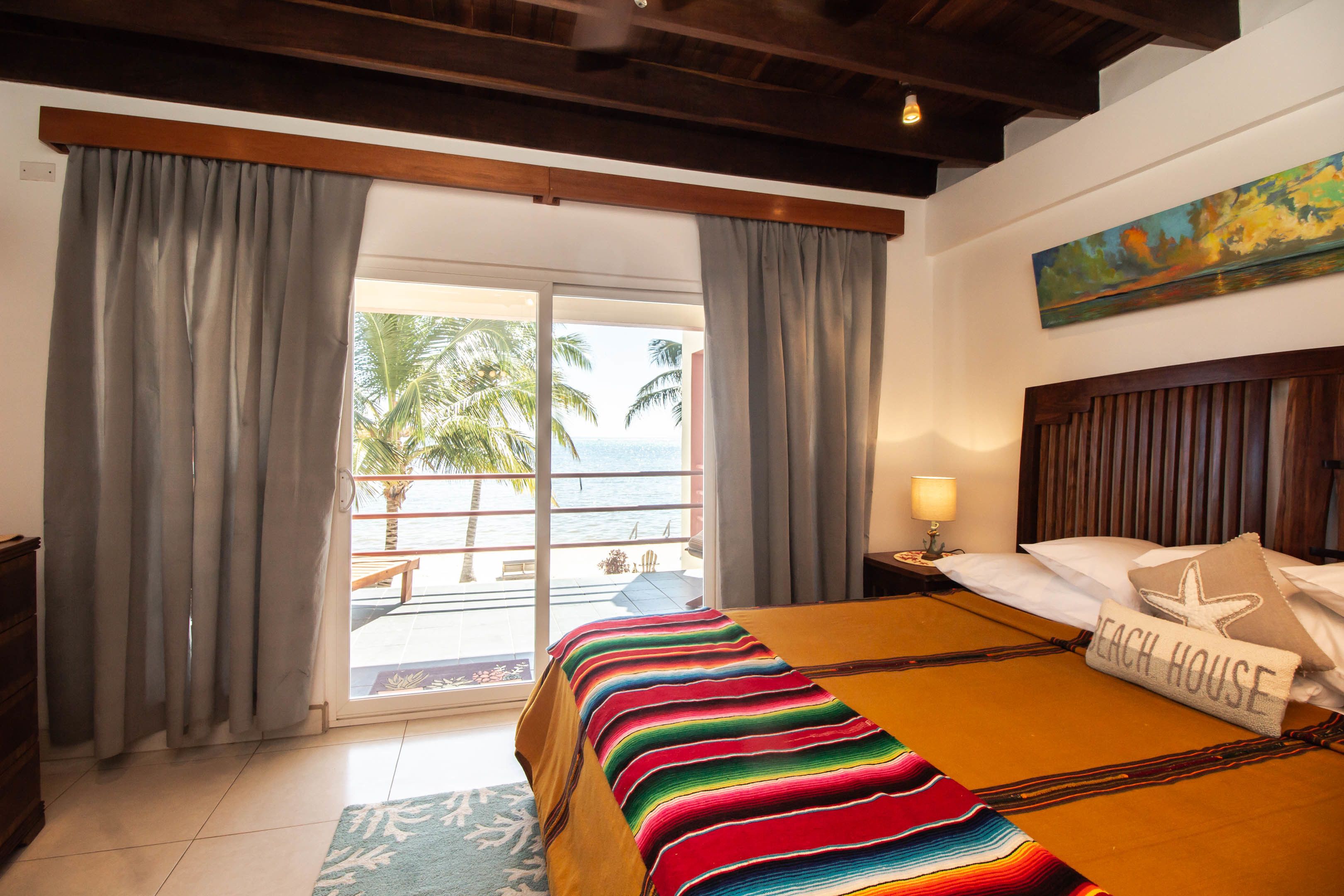 A hotel room with a large bed, a view of the ocean, and a balcony with curtains.
