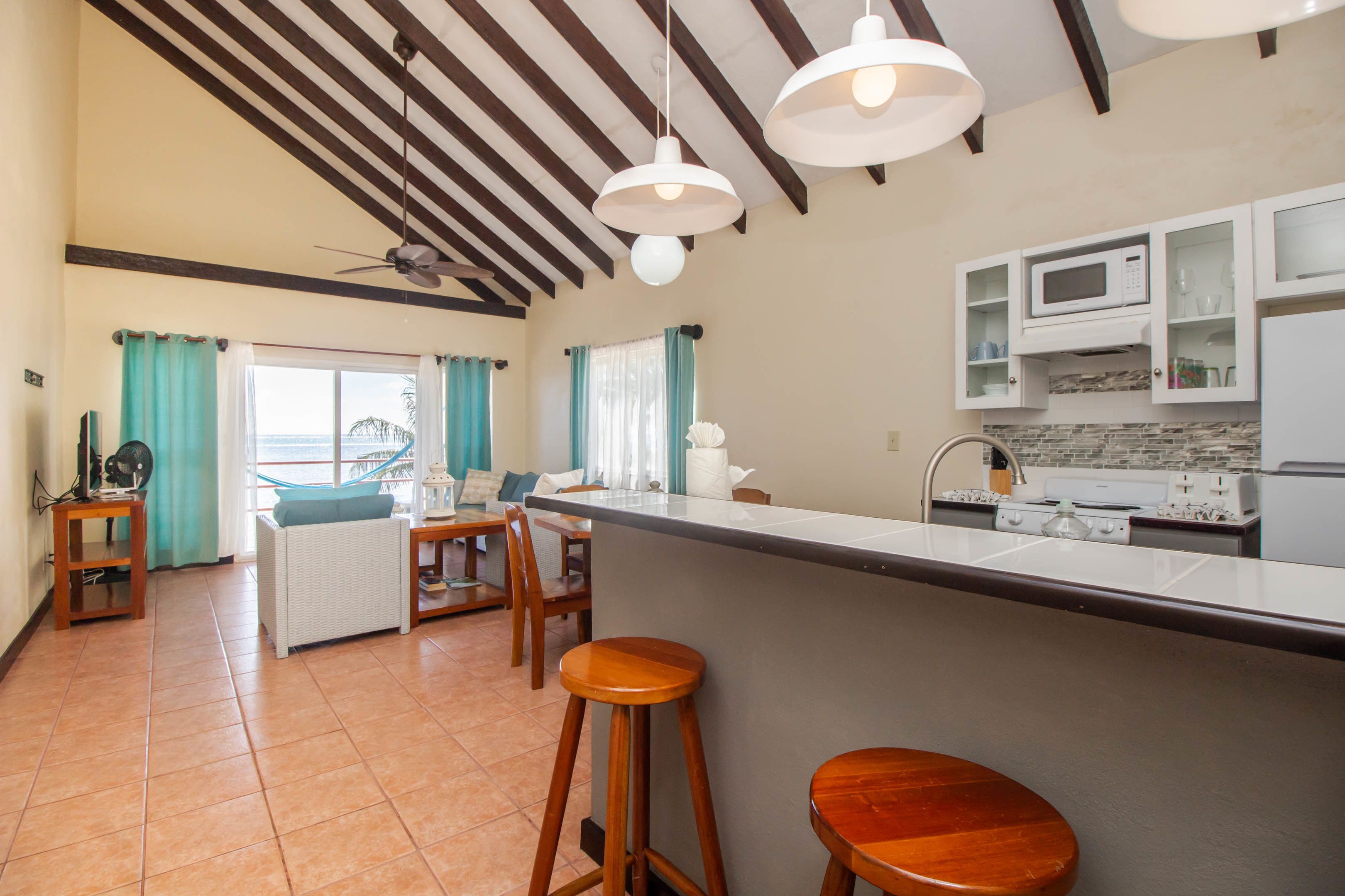 Una cocina con una isla central, taburetes de bar, un ventilador de techo y vista al océano.