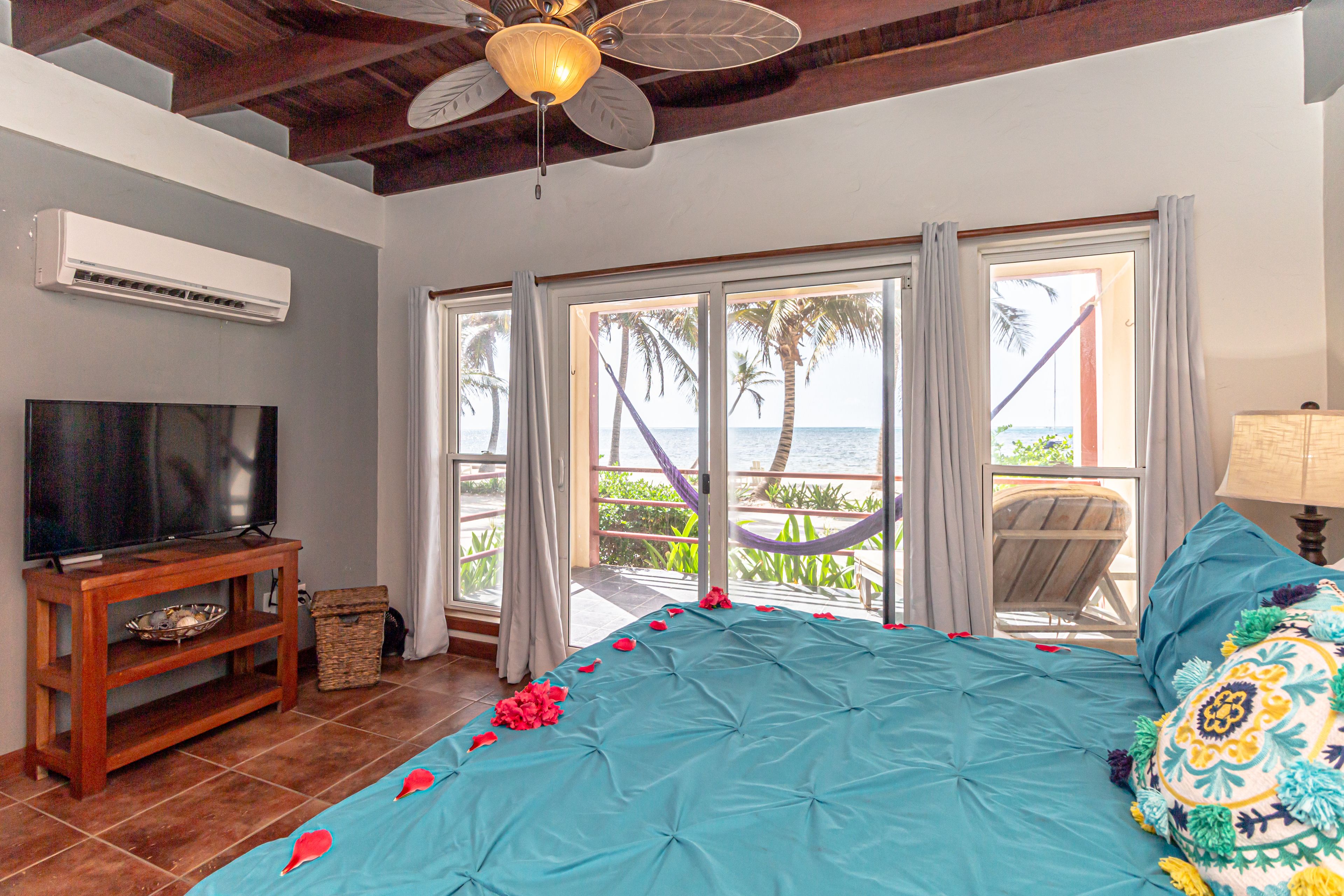 A bedroom with a bed, a TV, an air conditioner, and a view of the ocean.