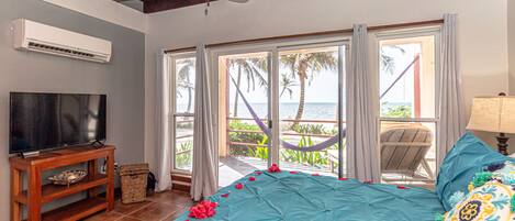 A bedroom with a bed, a TV, an air conditioner, and a view of the ocean.