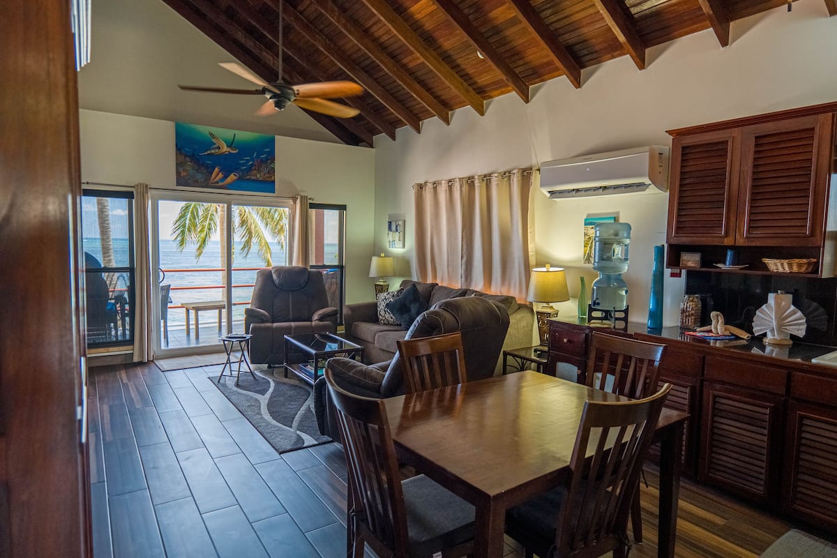 A spacious living area with a wooden ceiling, a dining table, and a kitchen area with wooden cabinets.