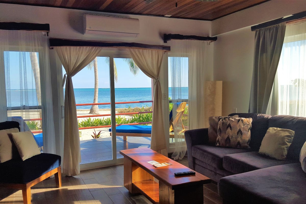 A room with a view of the beach, a sofa, a coffee table, and a chair.