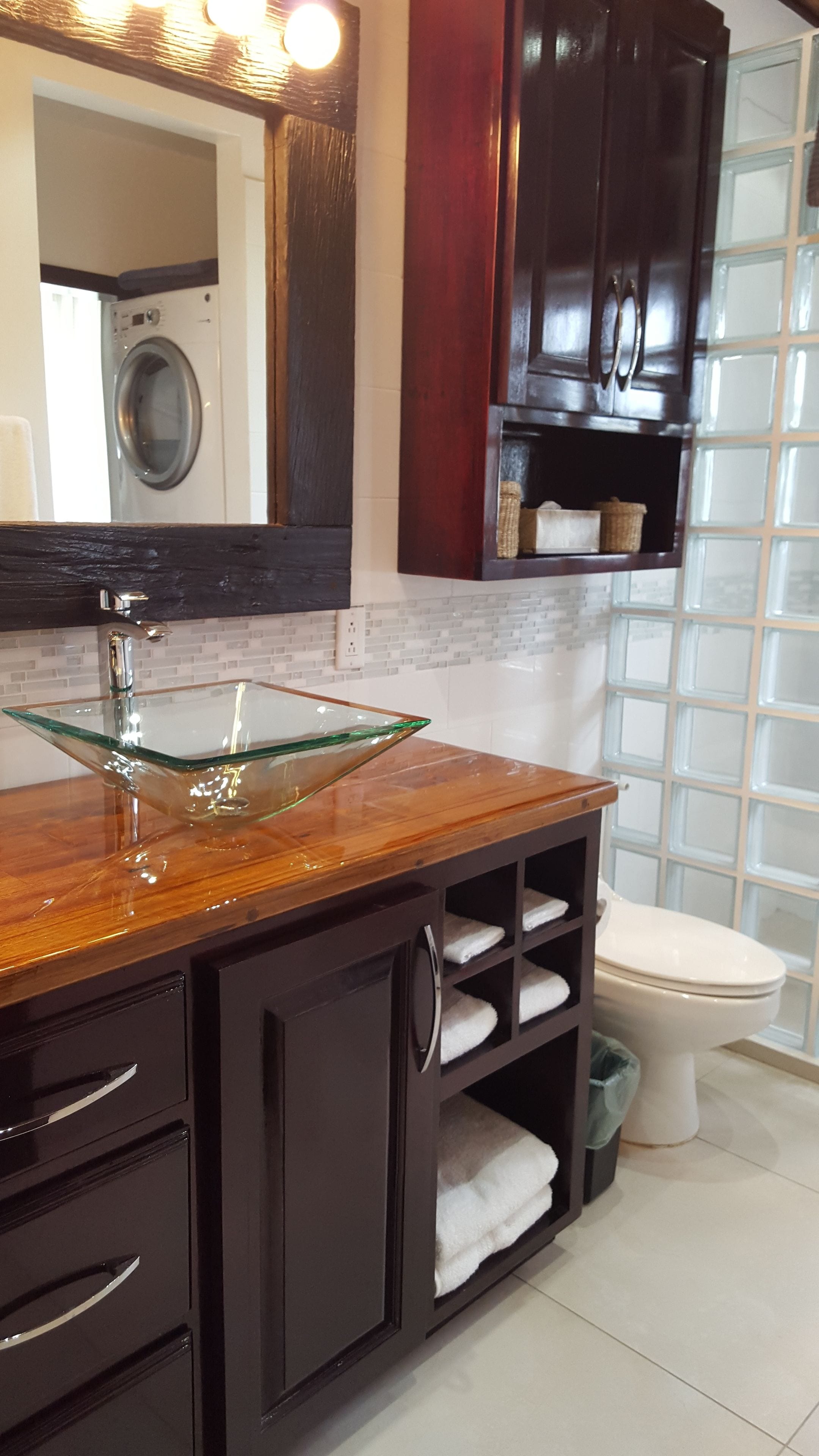 A bathroom with a glass sink, dark wooden cabinets, a white toilet, and a tiled shower area.