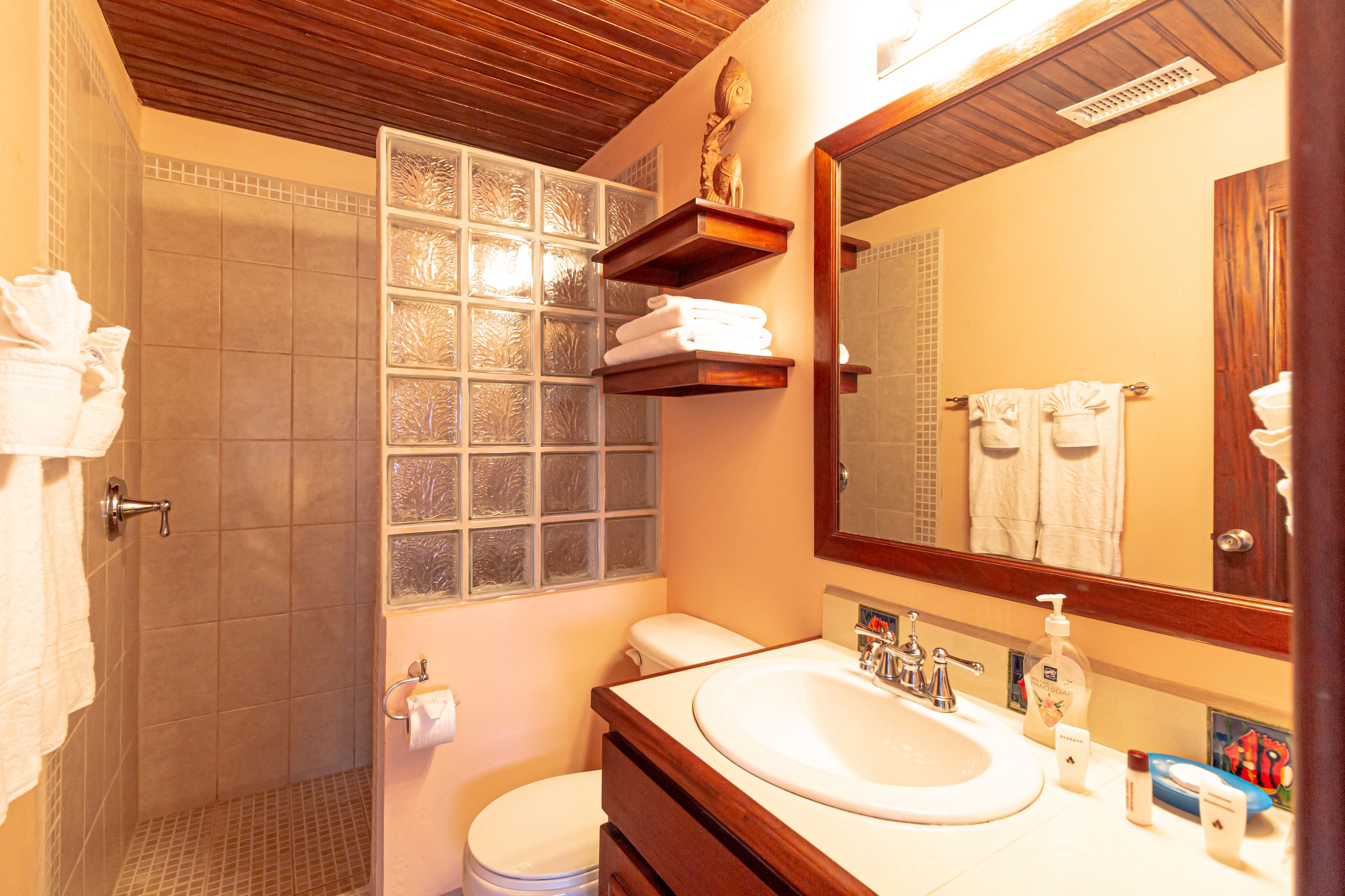 A bathroom with a shower, toilet, sink, and a mirror.