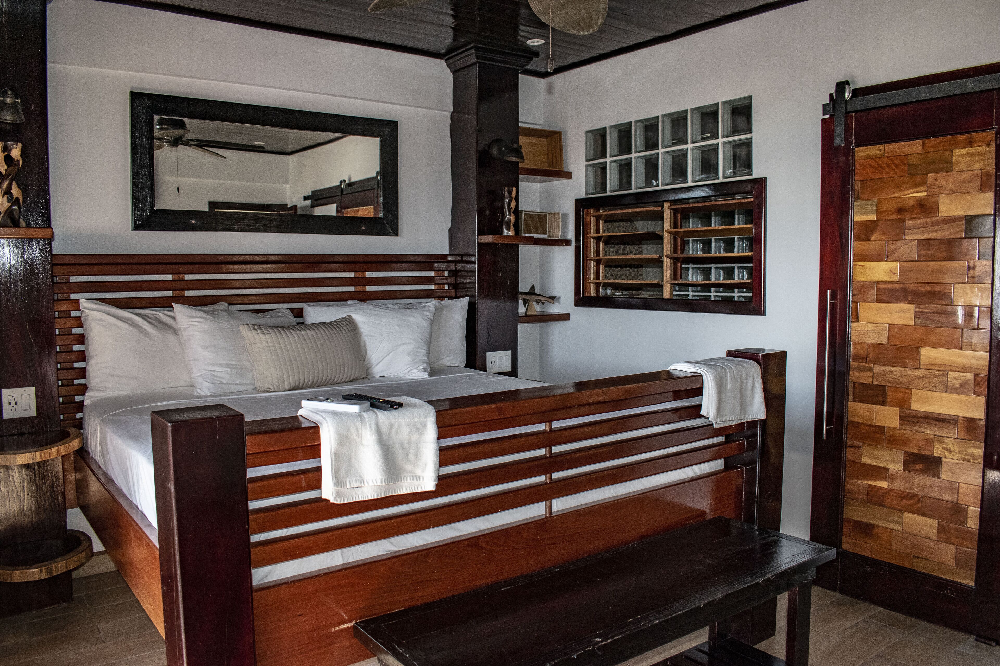 Een houten bed met hoofdeinde, nachtkastje, bankje, spiegel en een plank met glazen.