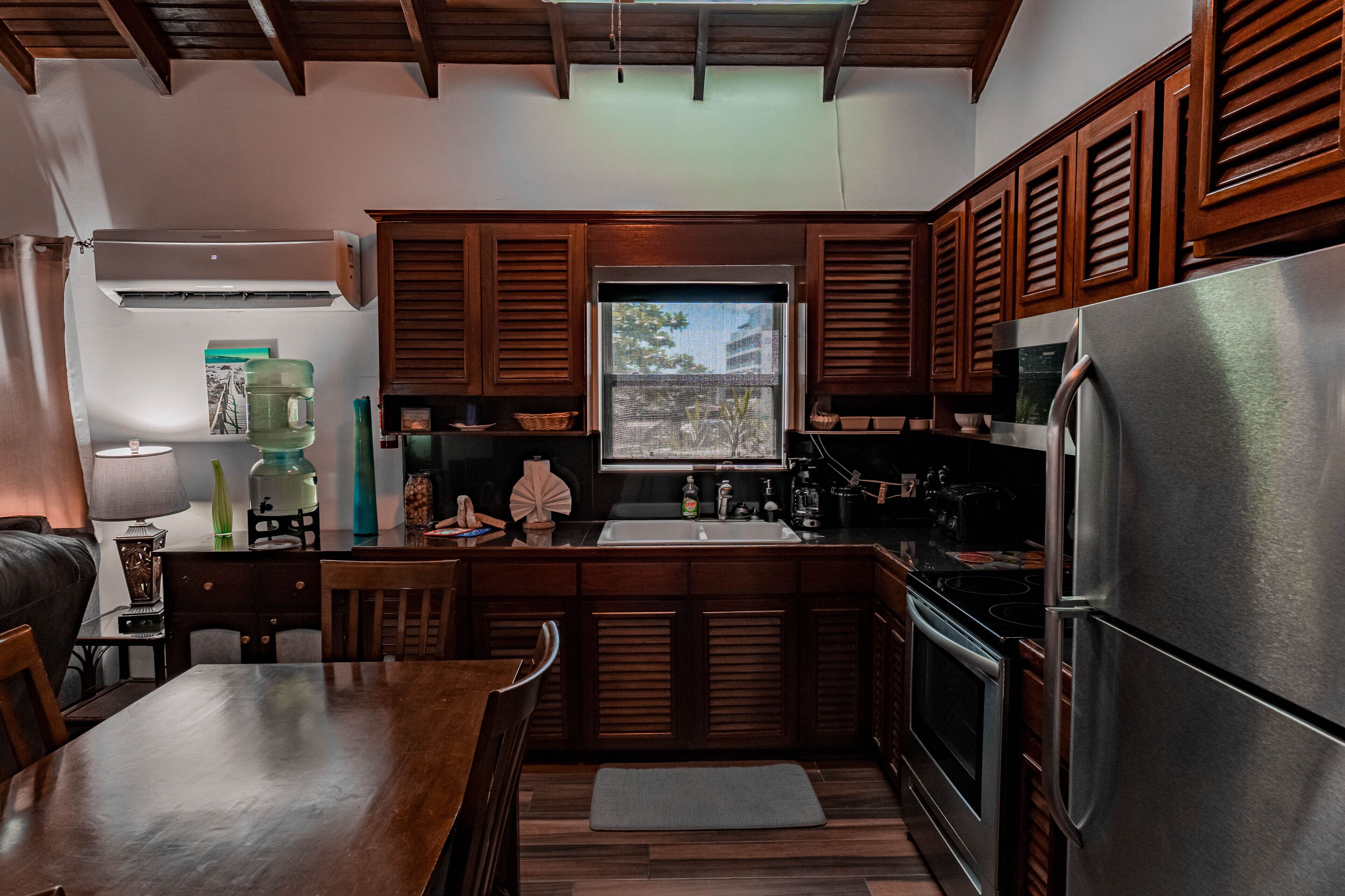 A kitchen with wooden cabinets, a stainless steel refrigerator, a window with a view, and a dining area with a table and chairs.