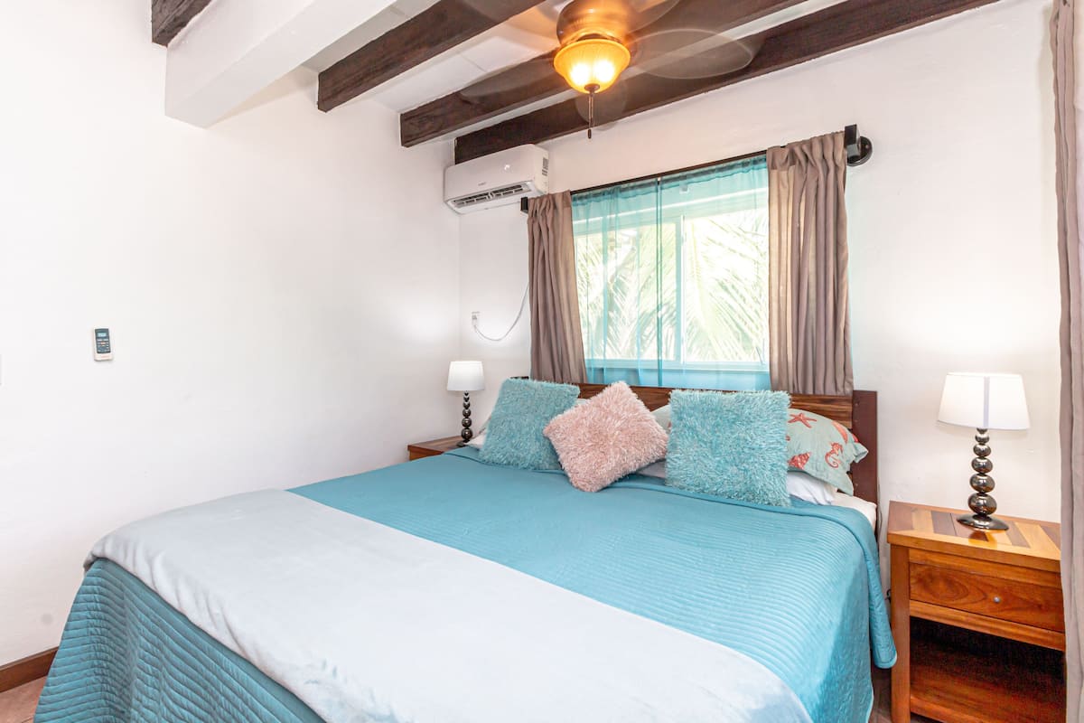 A bedroom with a bed, a nightstand, a ceiling fan, and a window with curtains.