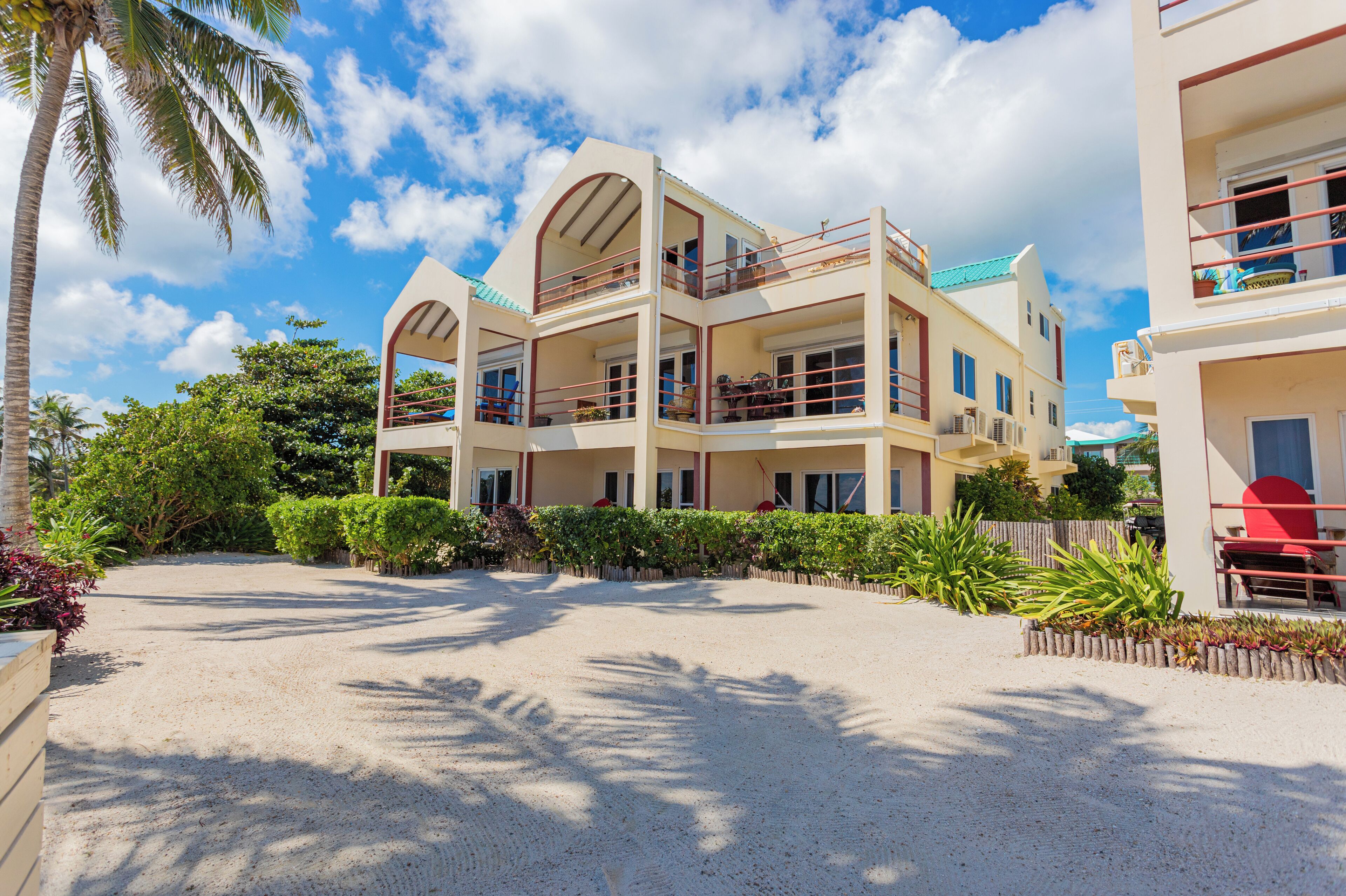 A multi-story hotel with balconies, a sandy driveway, and tropical landscaping.