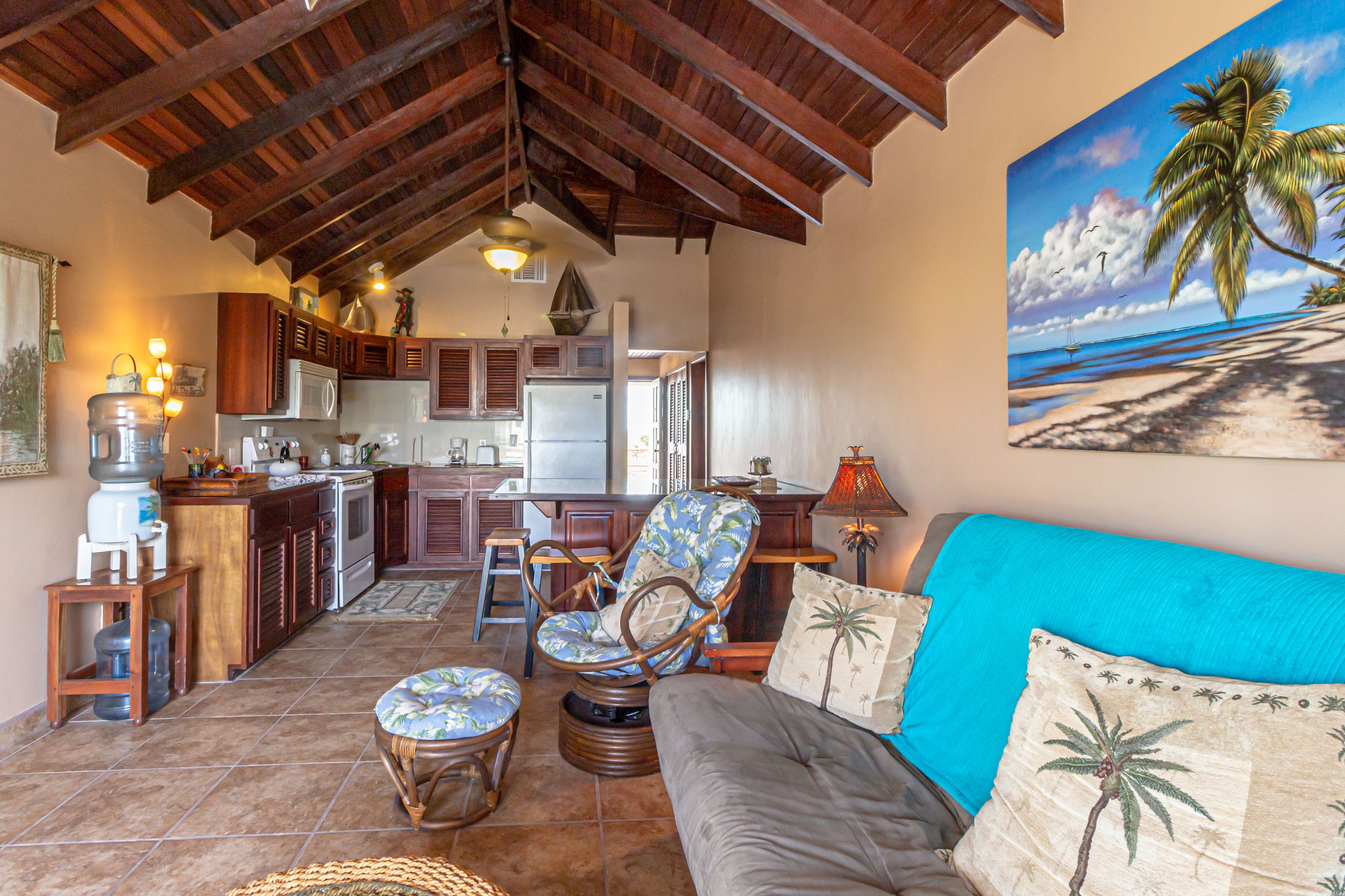 Una sala acogedora con un sofá, una silla y una mesa de comedor. Se ve una cocina al fondo con armarios y un refrigerador.