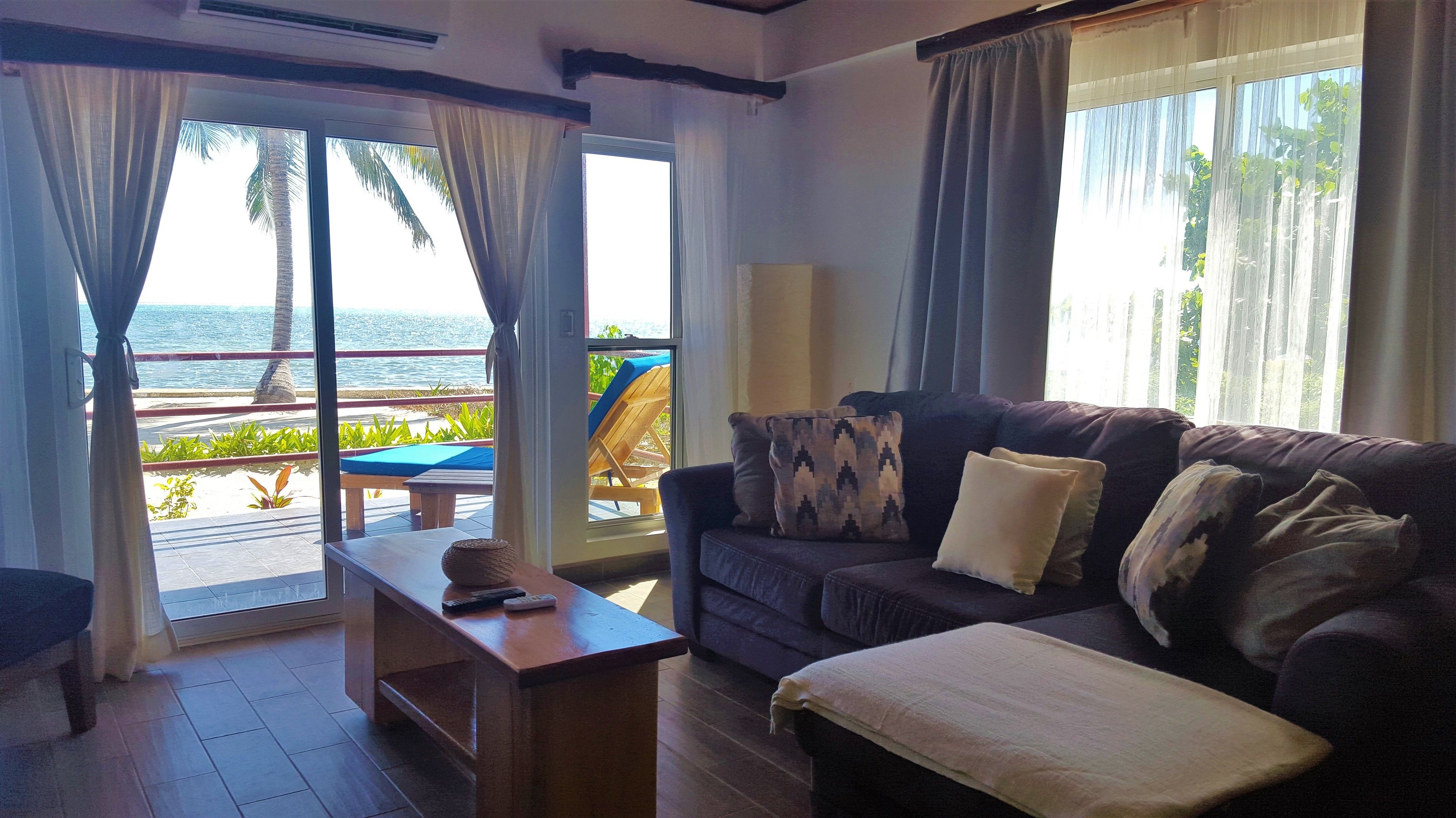 A living room with a couch, a coffee table, and a view of the beach through large windows.
