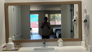 A bathroom with a large mirror, a sink, and a hairdryer on the wall. - Cali Inn (Carson)