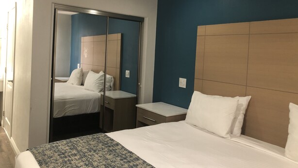 A hotel room with a bed, bedside table, and a wardrobe with a mirror. - Cali Inn (Carson)