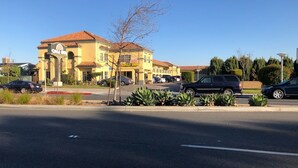 A yellow building with a red-tiled roof, likely a hotel, with a parking lot in front. - Cali Inn (Carson)