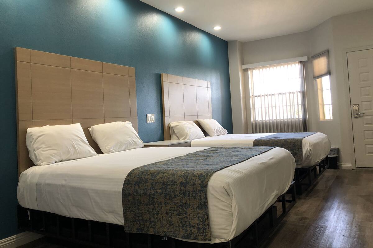 Una camera d'albergo con due letti, una parete blu e un poggiatesta in legno.