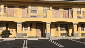 A two-story building with a yellow facade, multiple windows, and a parking lot in front. - Cali Inn (Carson)