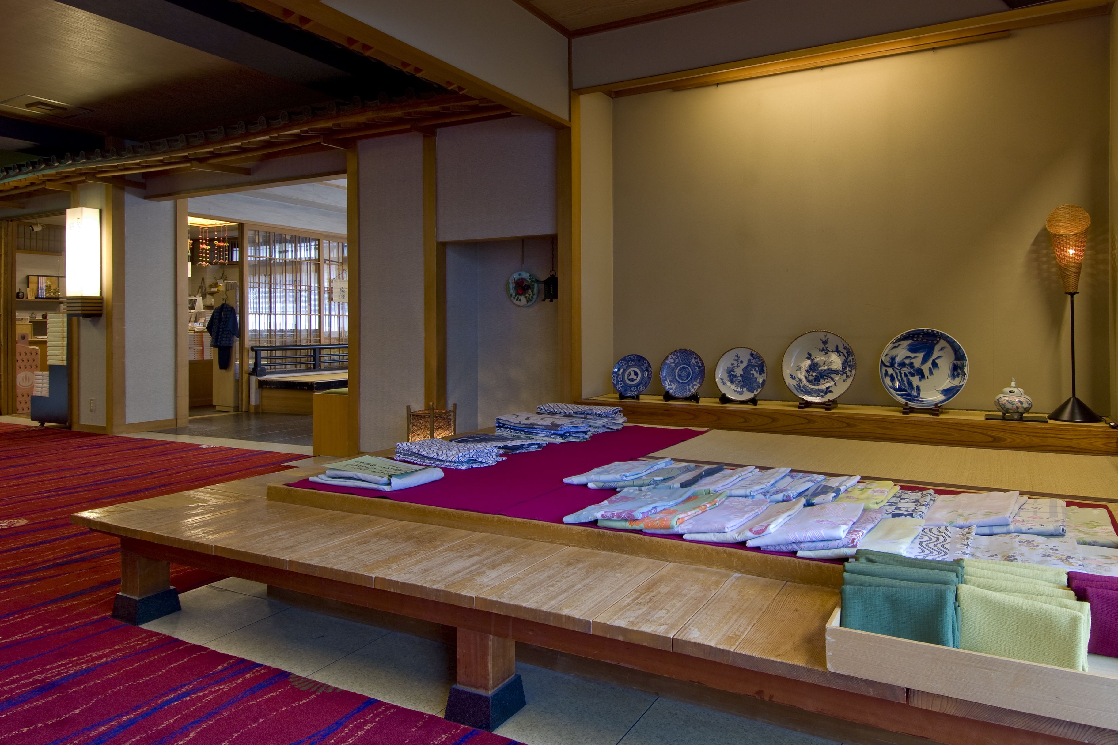 Una habitación japonesa tradicional con esteras de tatami, una mesa de madera con textiles y una pared que exhibe platos de porcelana azul y blanca.