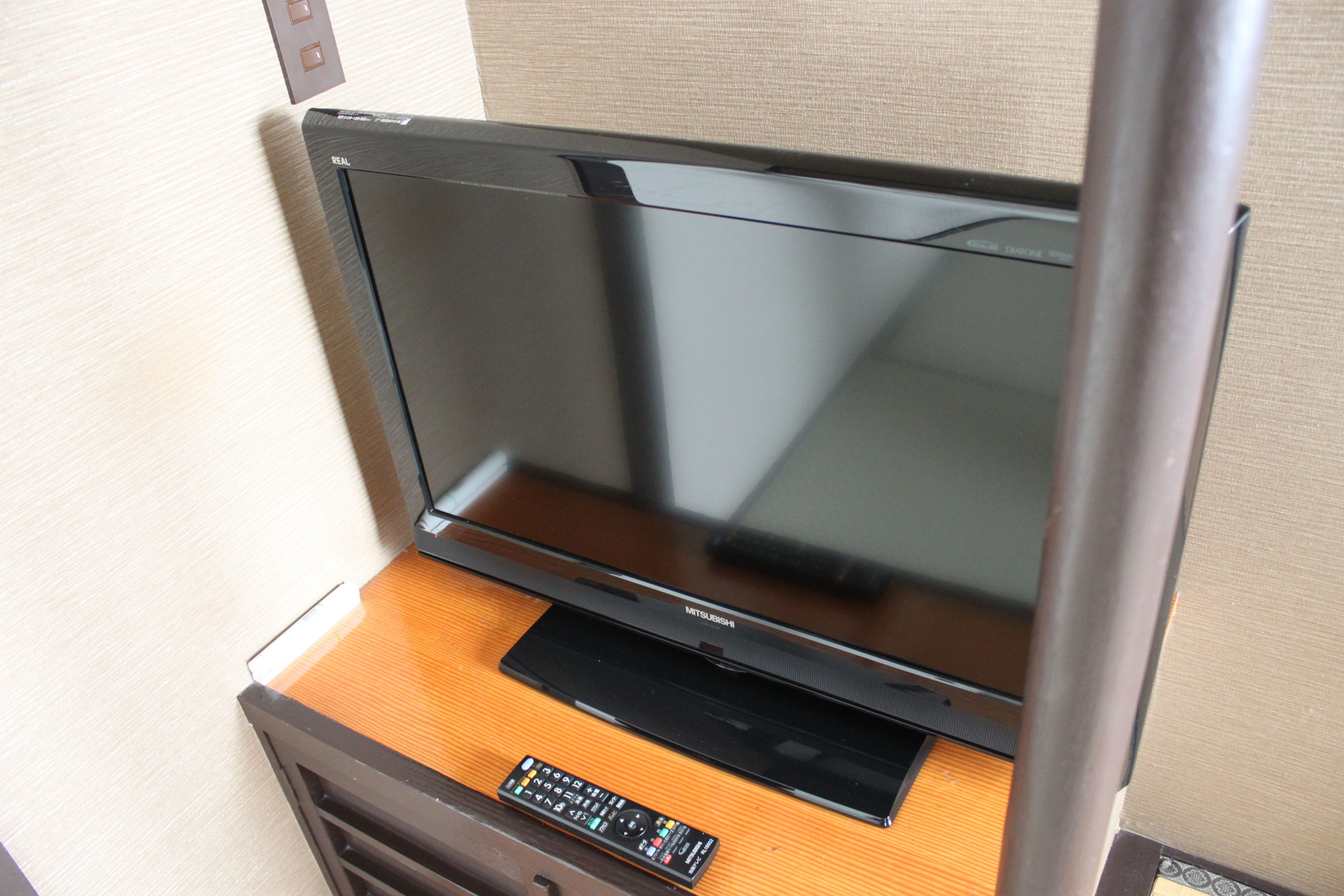 A flat-screen TV mounted on a wooden cabinet with a remote control on the cabinet's surface.