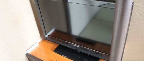 A flat-screen TV mounted on a wooden cabinet with a remote control on the cabinet's surface.