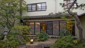 Un edificio tradicional al estilo japonés con jardín, faroles de piedra y un pasillo de madera.