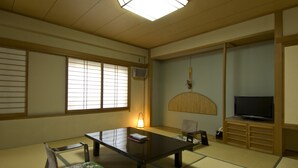 Una habitación japonesa tradicional con suelo de tatami, una mesa baja, un sofá, un televisor y una puerta corredera.